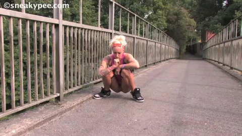 Blonde chick pees on bridge, checks out small object on ground