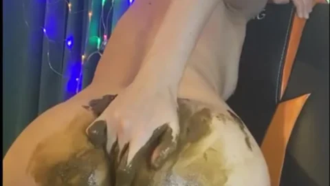 Slim brunette bends over chair applying mud mask to ass