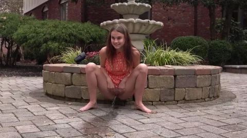 Teen brunette pisses on stone planter in outdoor daylight scene