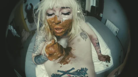 Blonde with tattoos eats and smears feces in fisheye bedroom scene